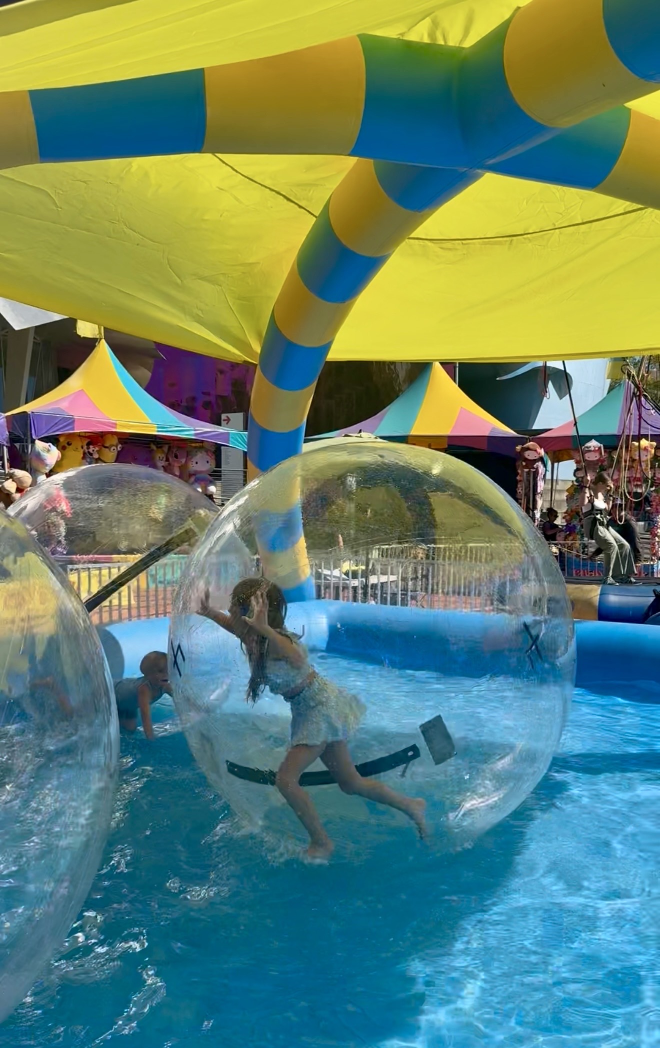 Girl laughing inside a giant water walking ball at a colorful outdoor event